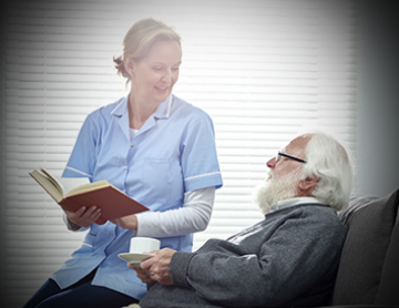 Female carer holding a book sitting on sofa with senior man